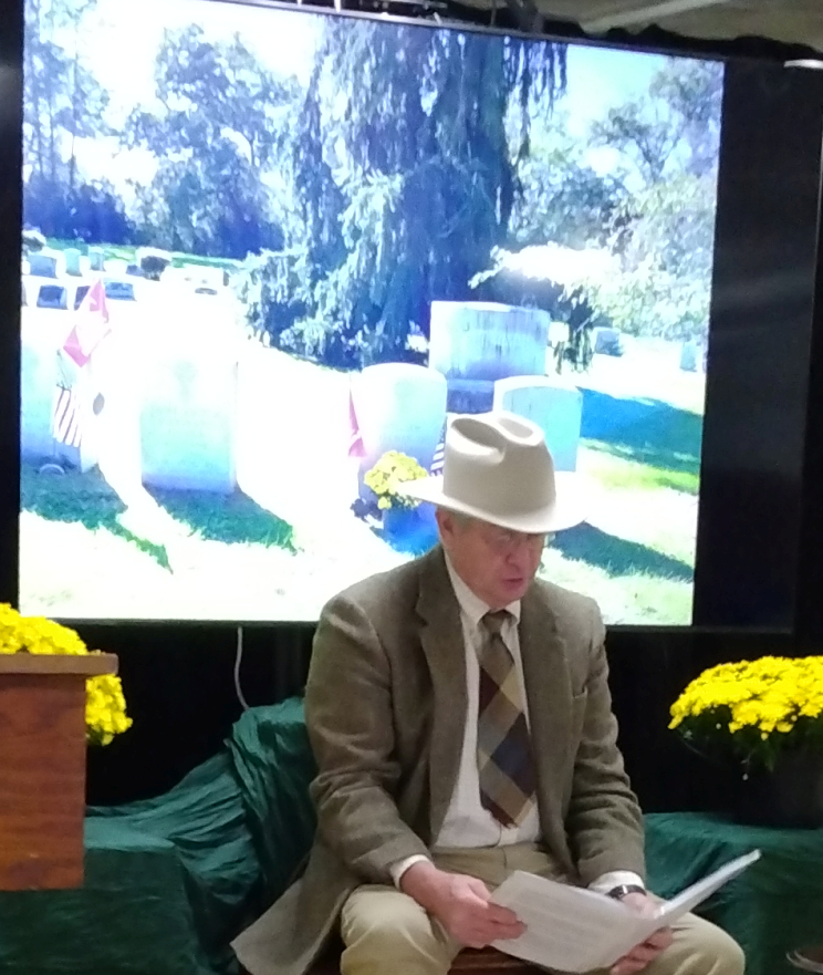 Planter in hat sits before photo of grave "Flemer"